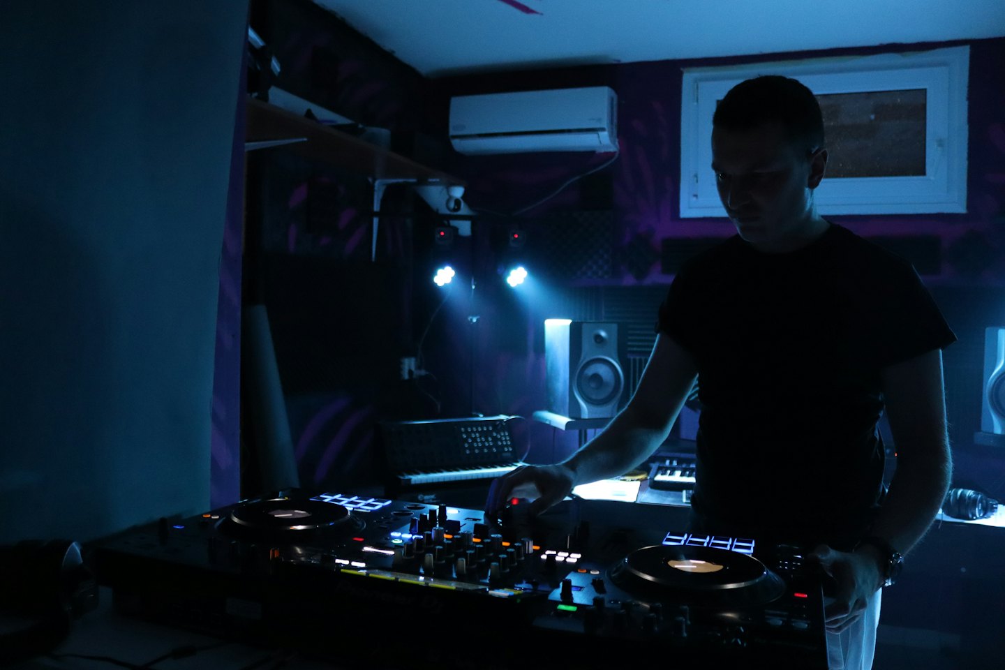 Młody mężczyzna miksujący muzykę na kontrolerze DJ-skim w klubie.