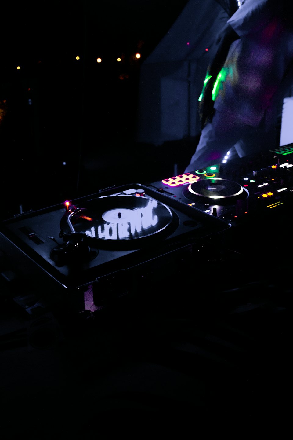 DJ miksujący muzykę na gramofonach przy kolorowych światłach.