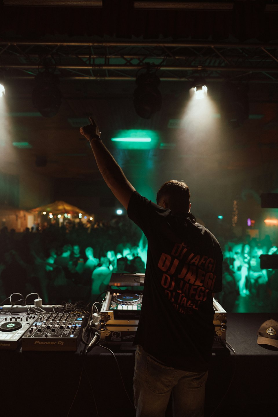 DJ z uniesionym ramieniem nad sprzętem nagłośnieniowym podczas nocnego wydarzenia.